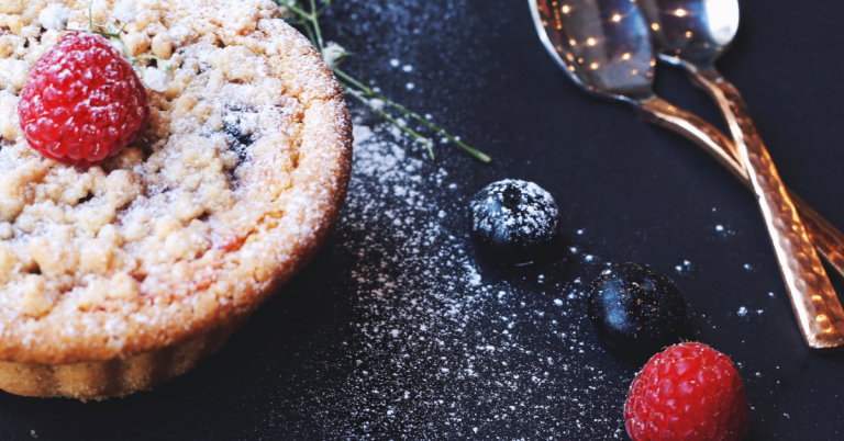 raspberry tart on table next to gold utensils